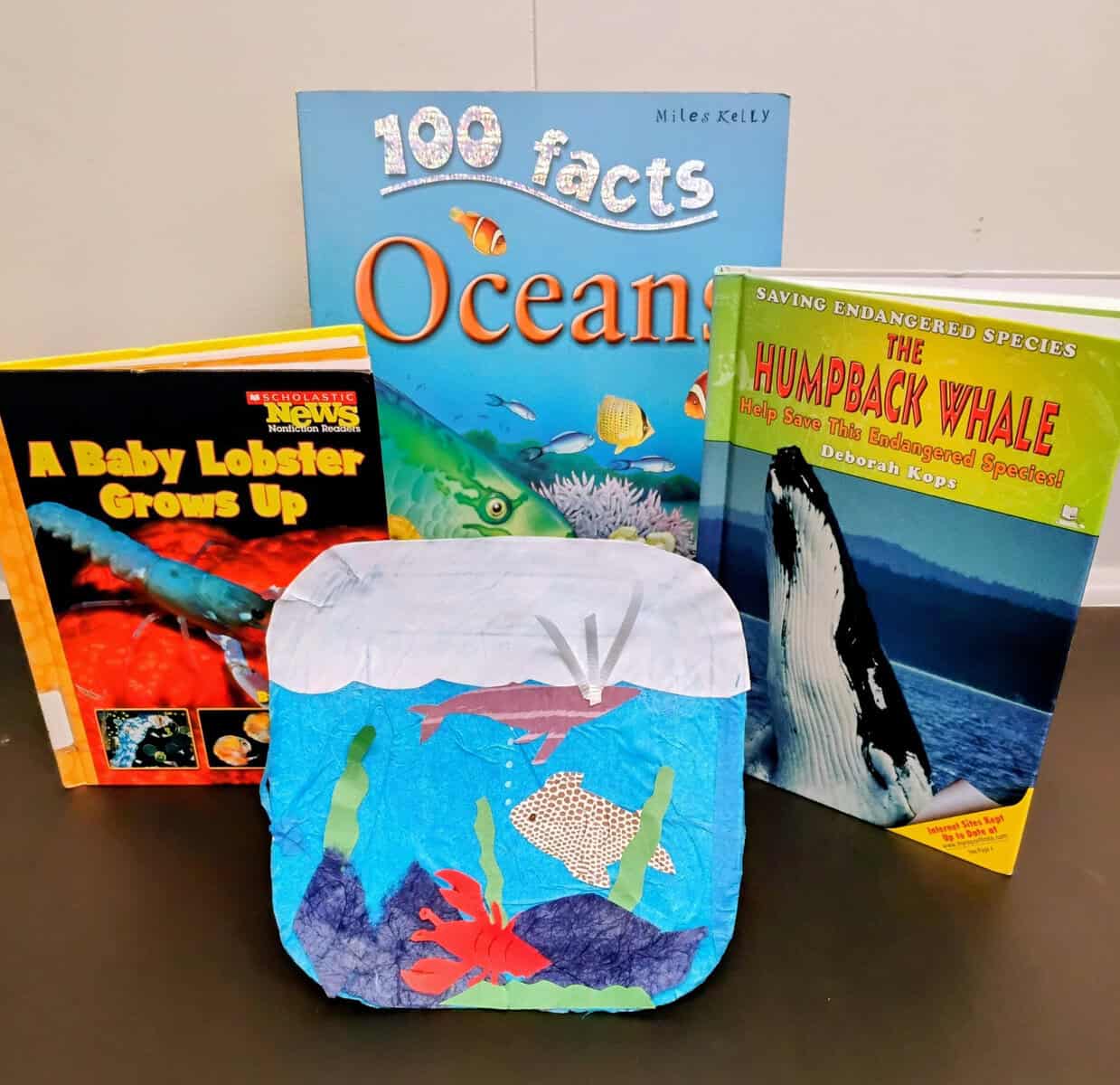 A paper craft scenery of underwater creatures. Behind the scene are children's books about oceans and ocean animals.