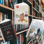 The covers of the book The Curious Incident of the Dog in the Night-Time, All the Quiet Places, and My Brilliant Friend. Behind the covers are shelves of books.