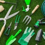 A collection of outdoor tools like shears, a garden hose, etc. all laid out on the grass. They are all shades of green.