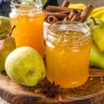 Two jars of pear jam. They are surrounded by pears, cinnamon sticks, and star anise.