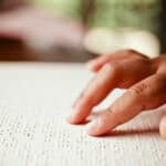 A child's hand reading the letters in a braille book.