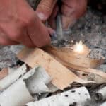 A pair of hands starting a fire with thin strips of wood and sticks. The photo captures the first spark.