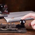 A hand using an old fashioned morse code machine to send a message. Beside it is a notebook and pen for writing down responses.