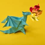 A green origami dragon. It has red, orange, and yellow flames made of paper.