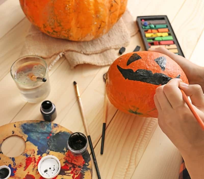 A child painting a black Jack-O-Lantern smile on a small pumpkin.