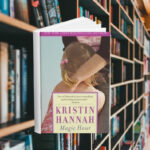 The cover features a small girl with pigtails hugging a woman's legs faced away from the camera. The woman leans down to hold her. Behind the cover are shelves of books.