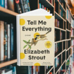 The cover features two medium sized birds on a branch looking at each other. Behind the cover are shelves of books.